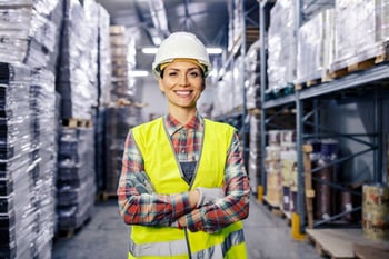Woman wearing hard hat in warehouse.