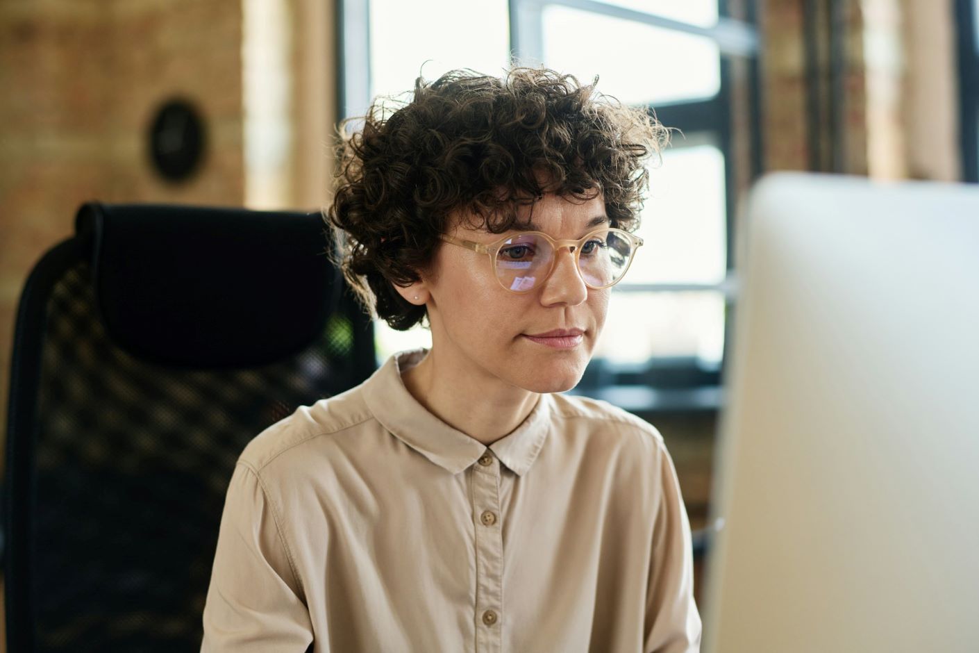 Woman with curly hair and glasses looking at laptop
