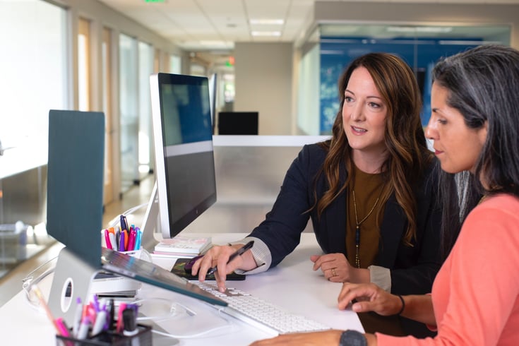 Two women engaged in work and talking at laptops